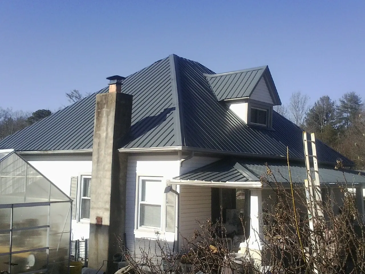 Dark blue standing seam metal roof on a white farmhouse with dormer — Slate & Tile Roof Repair by Roofing Brothers in Warner