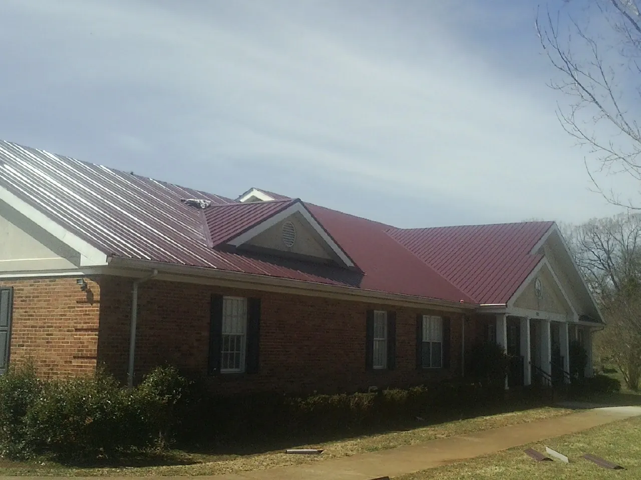 Red metal roof with gabled entries on a long brick building, from a Hail Damage Roof Repair job in Warner