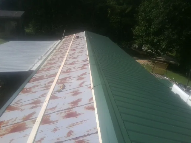 Old rusted panels beside newly installed green metal roofing — Wind Damage Roof Repair by Roofing Brothers in Warner