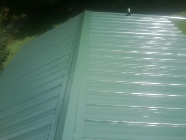 New green metal panels meeting at the ridge of a roof — Flat Roof Repair work by our crew in Warner