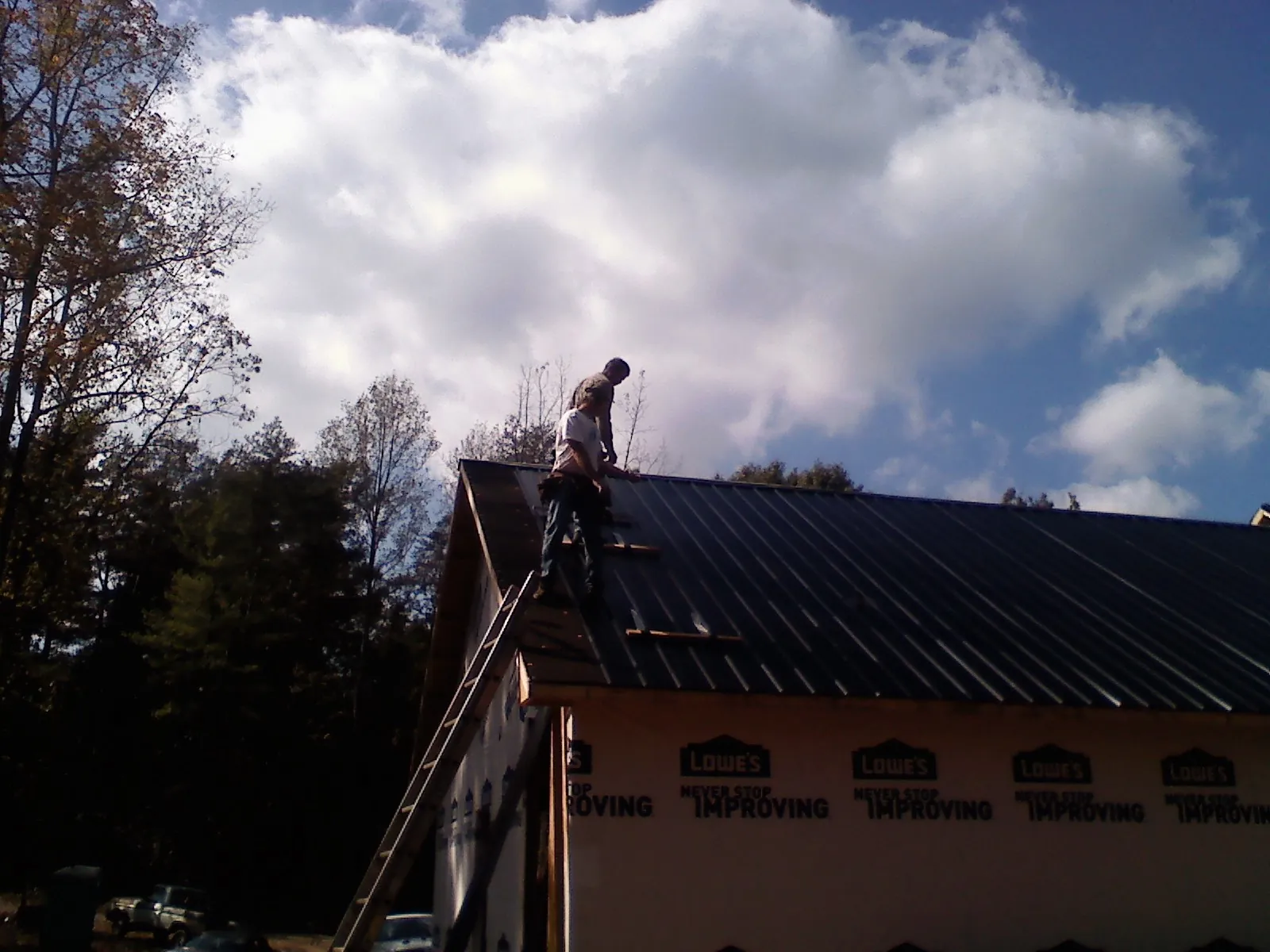 Roofer fastening dark metal panels high against a cloudy sky, from a Roof Inspection job in Warner