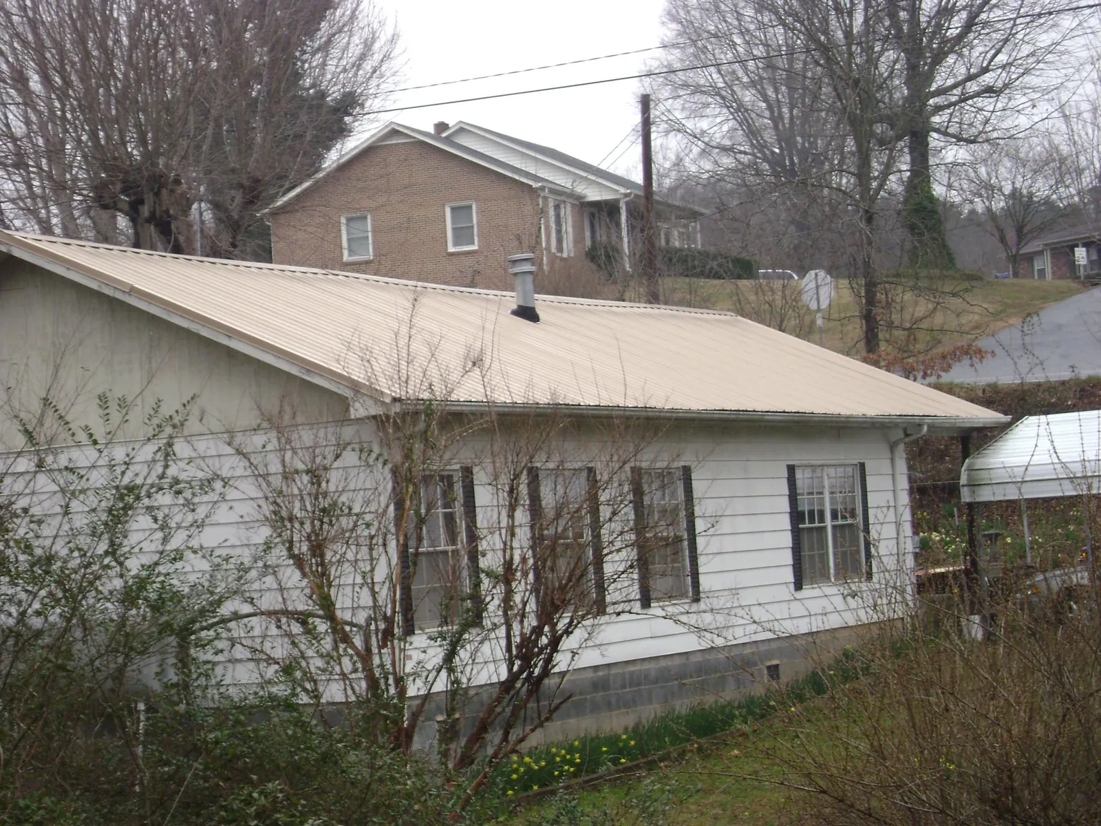 Tan metal roof on a white sided house set into a hillside — Commercial Roofing by Roofing Brothers in Warner