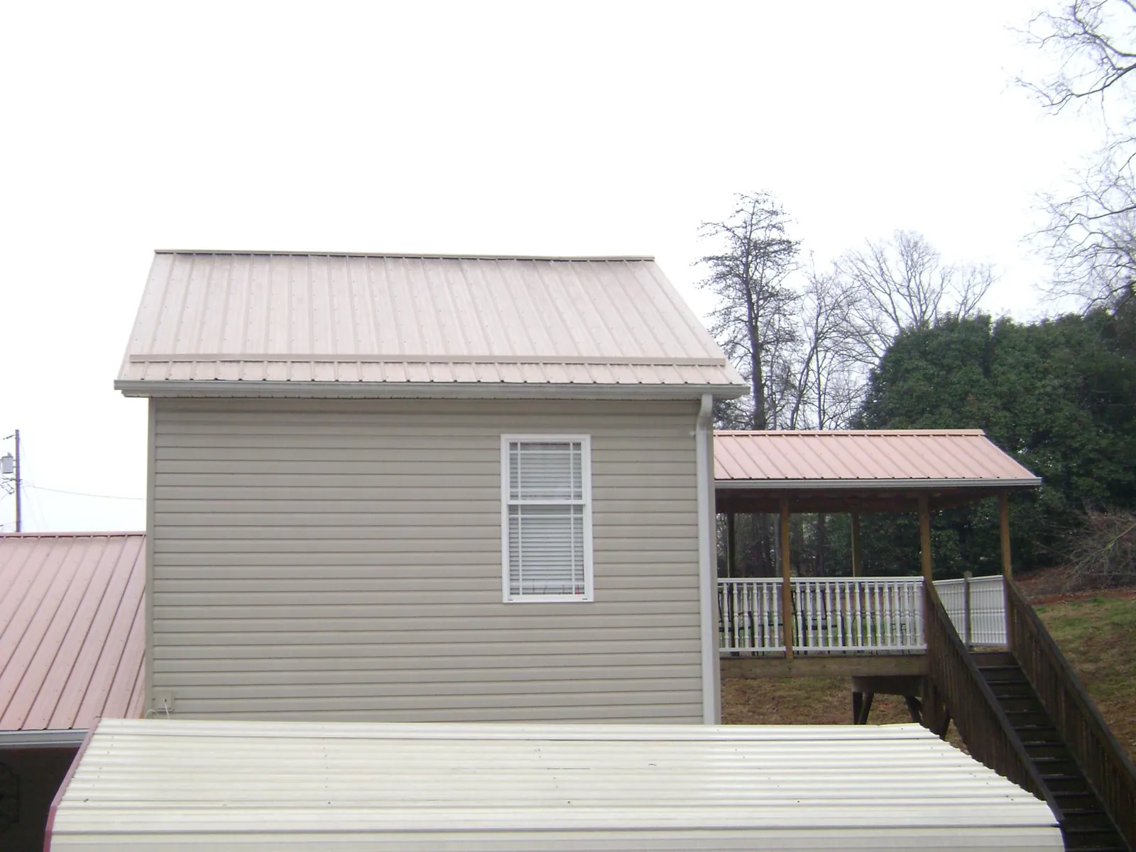 Tan metal roofs on a two story addition and attached porch, from a Roof Replacement job in Warner