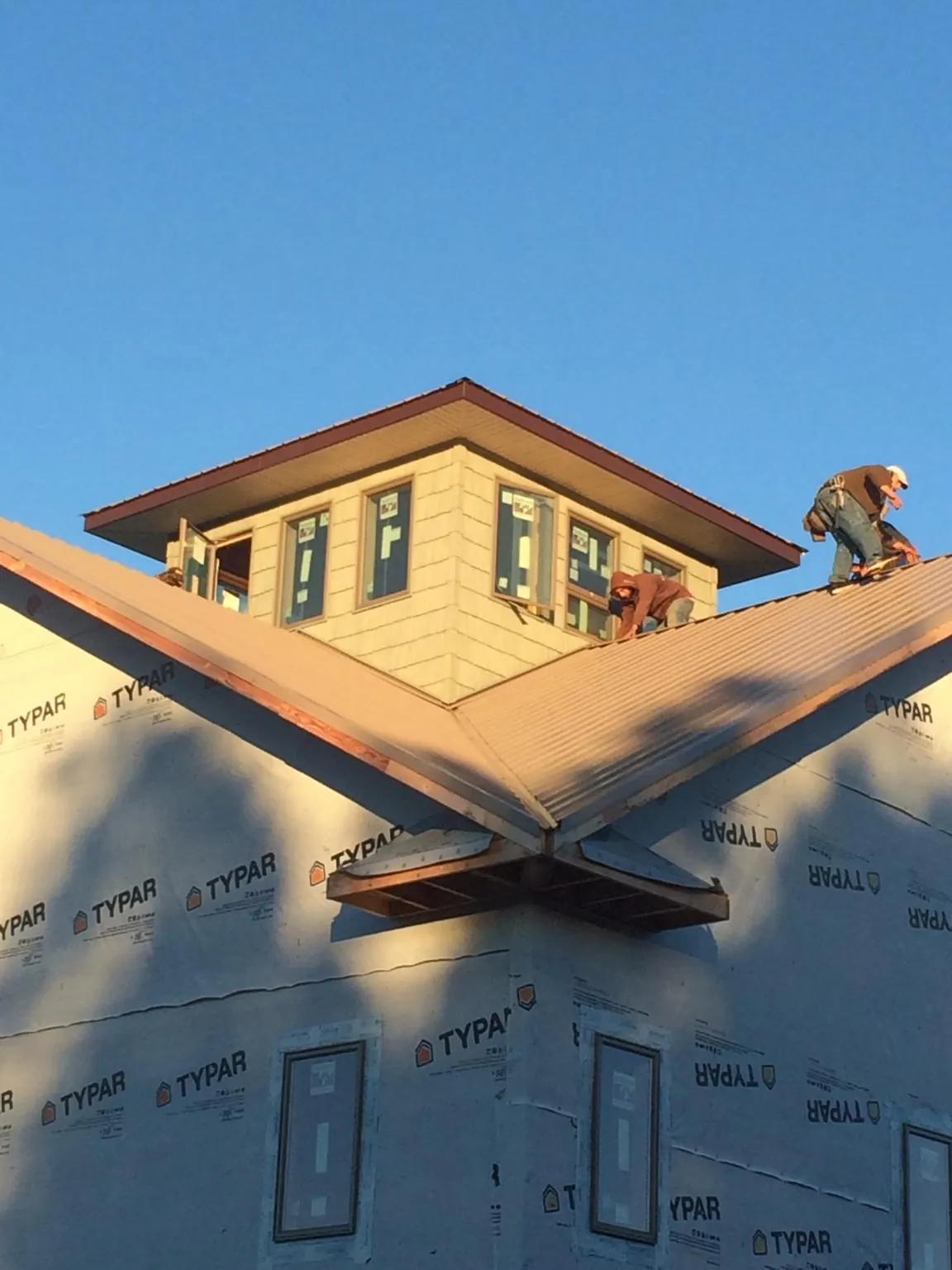 Roofers working around a rooftop cupola on a new metal roof at sunset — Roof Waterproofing in Warner by Roofing Brothers